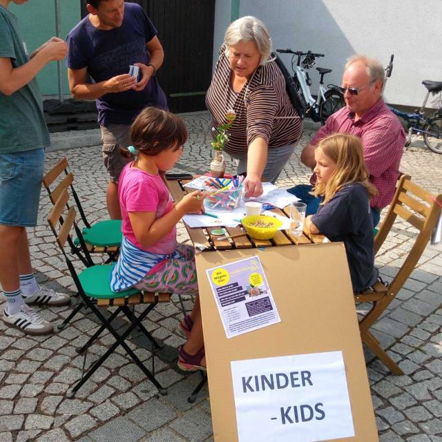 Kinder und Erwachsene basteln am Tisch mit Schild „Kinder – Kids“.